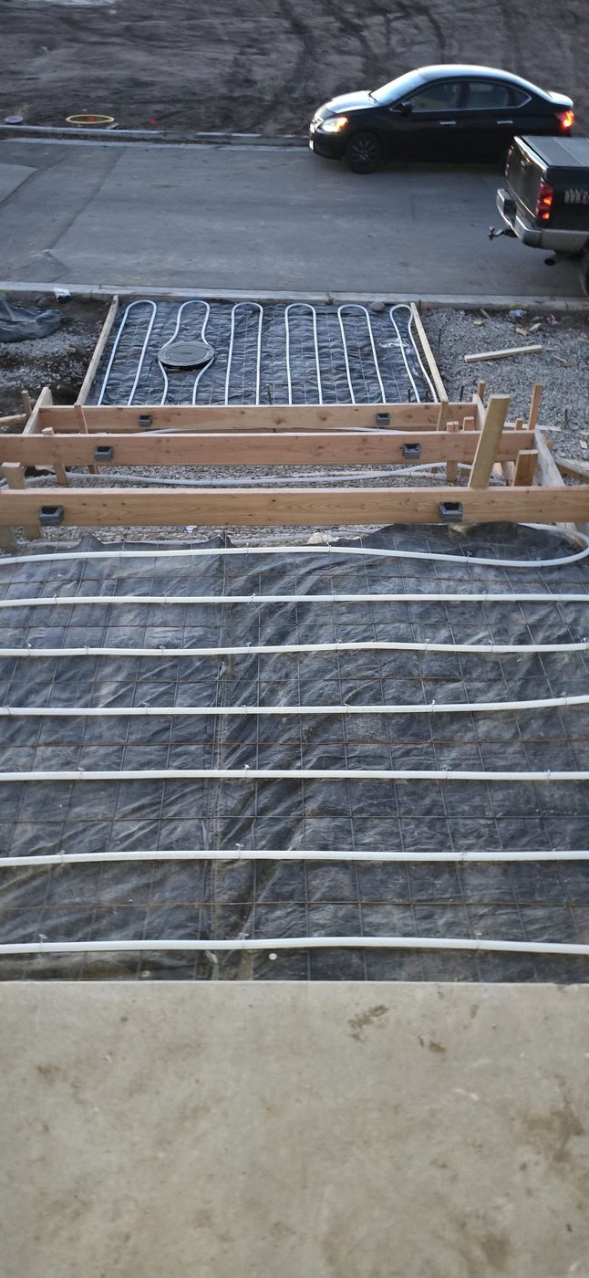 Snow-melt installation in progress showing PEX tubing tied to rebar grid over vapor barrier, before concrete pour